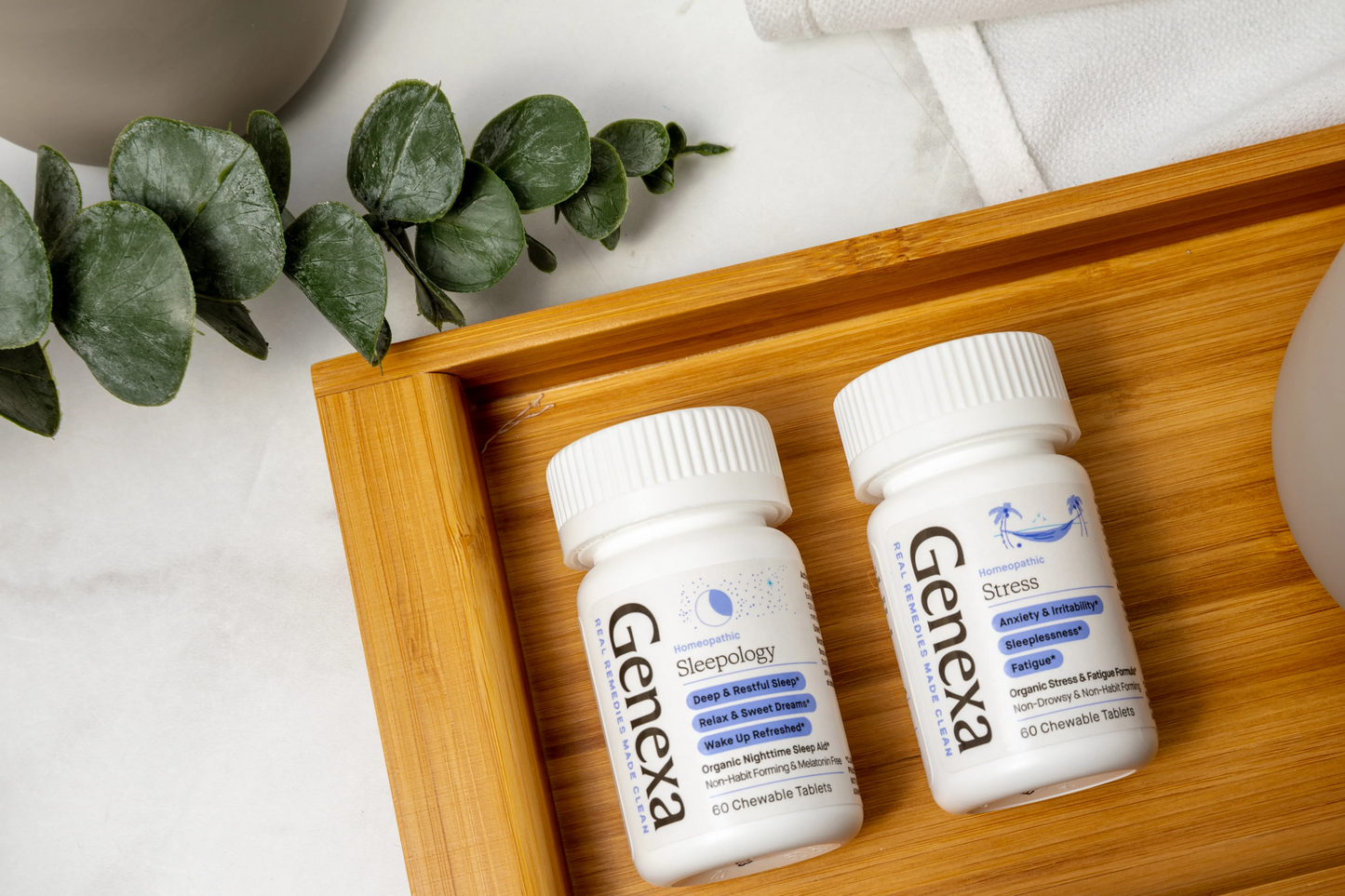 Two Genexa bottles on a wooden tray with a plant and mug in the background.
